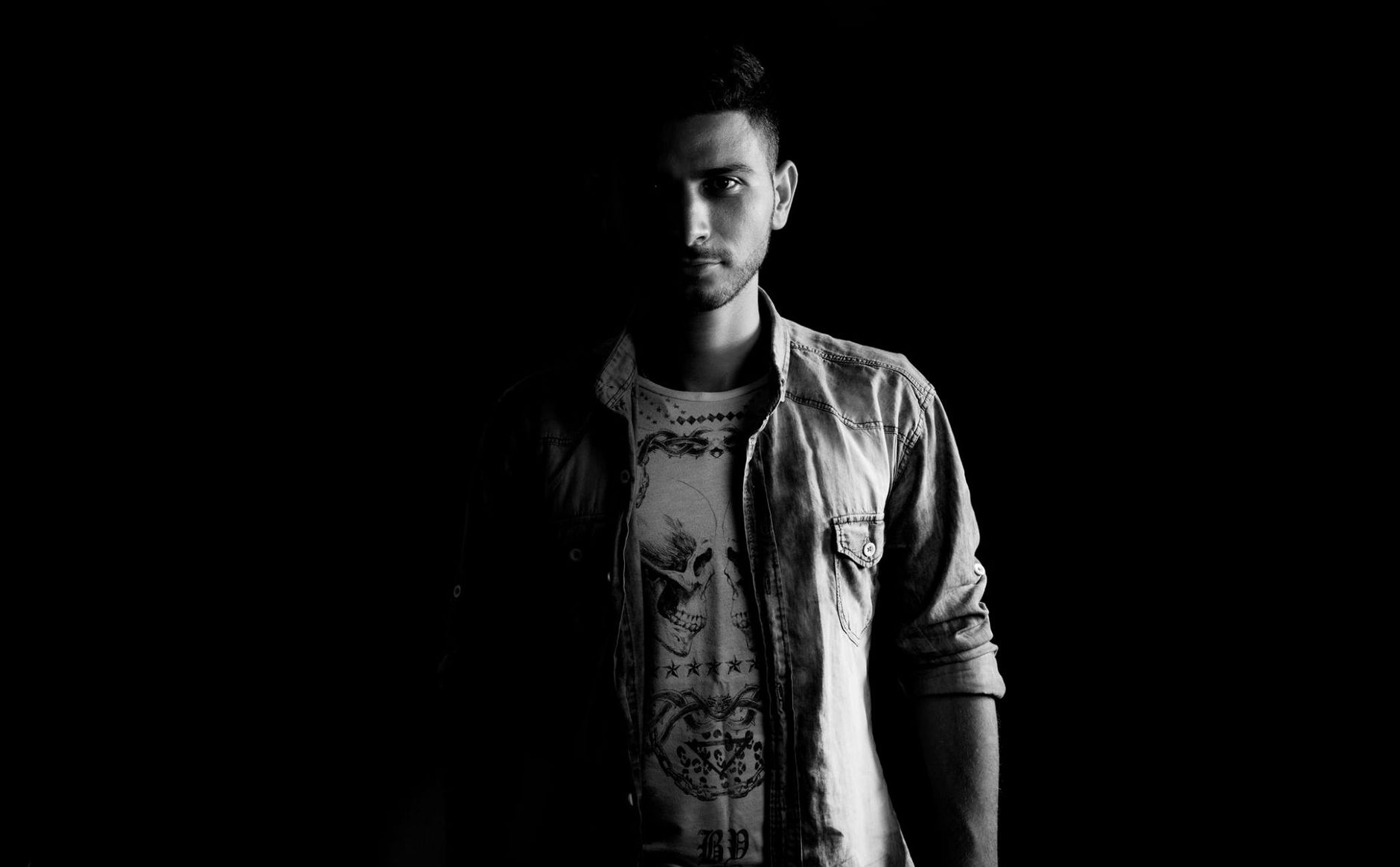 A dark printed tee/top on a real person in a dim room, framed chest-up-to-hem so the print graphic reads
