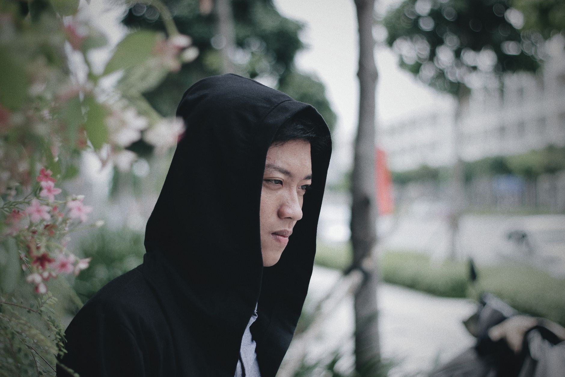 A black hoodie on a real person, hood up, shot three-quarter in a dark studio corner